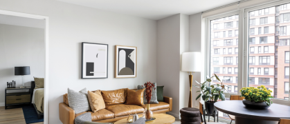 living room with brown leather sofa, white walls, & large windows looking out on another building